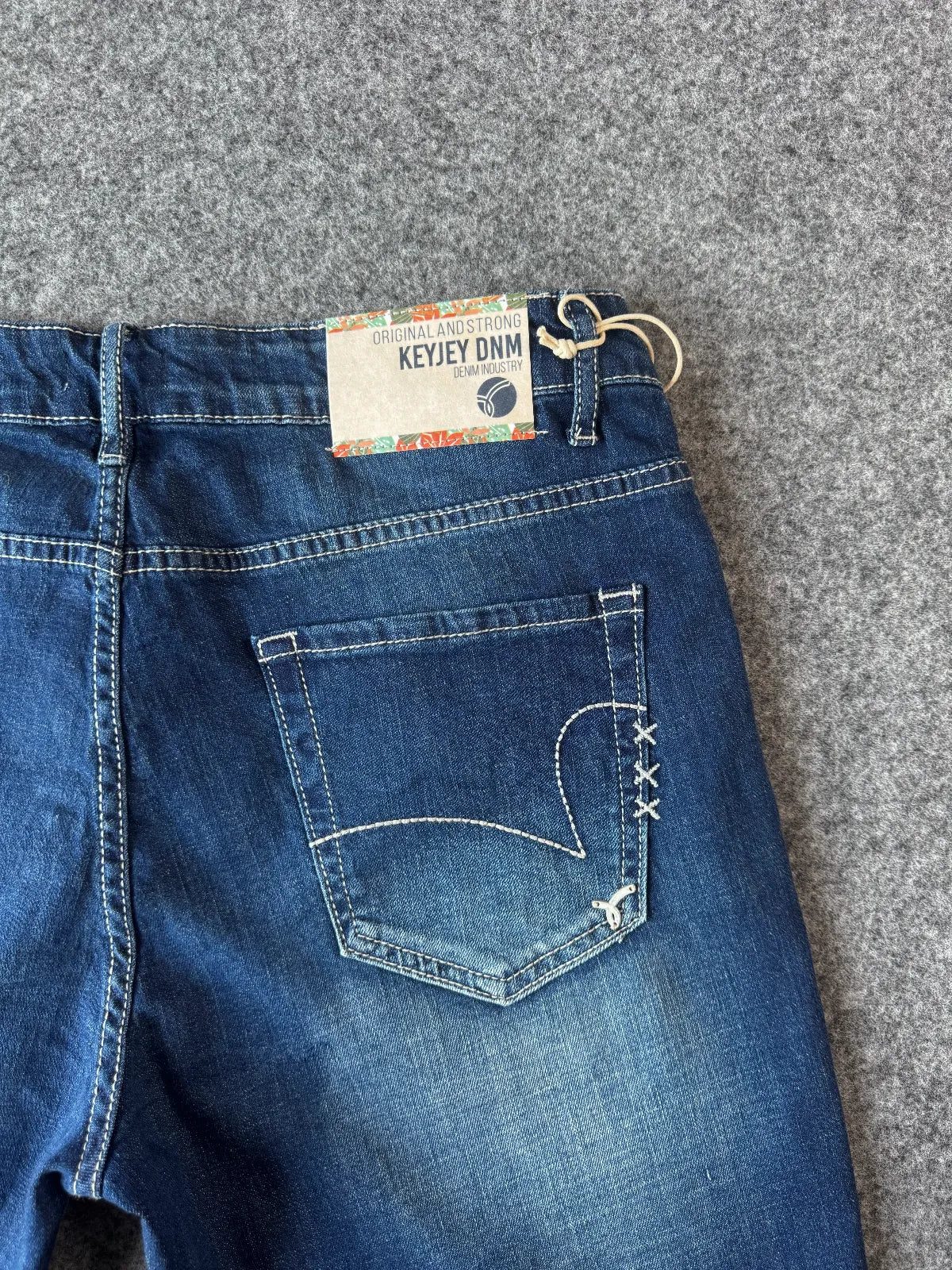 Dettagli patch logata e logo metallizzato posteriore bermuda di jeans blu - Archivio Tessile